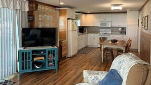 Un espacio habitable compacto con televisión, kitchenette, comedor y mueble de entretenimiento azul.