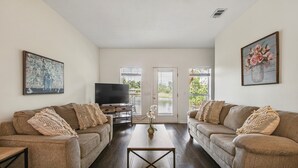 Ein Wohnzimmer mit zwei Sofas, einem Couchtisch, einem Fernseher und einer Tür, die nach draußen führt.