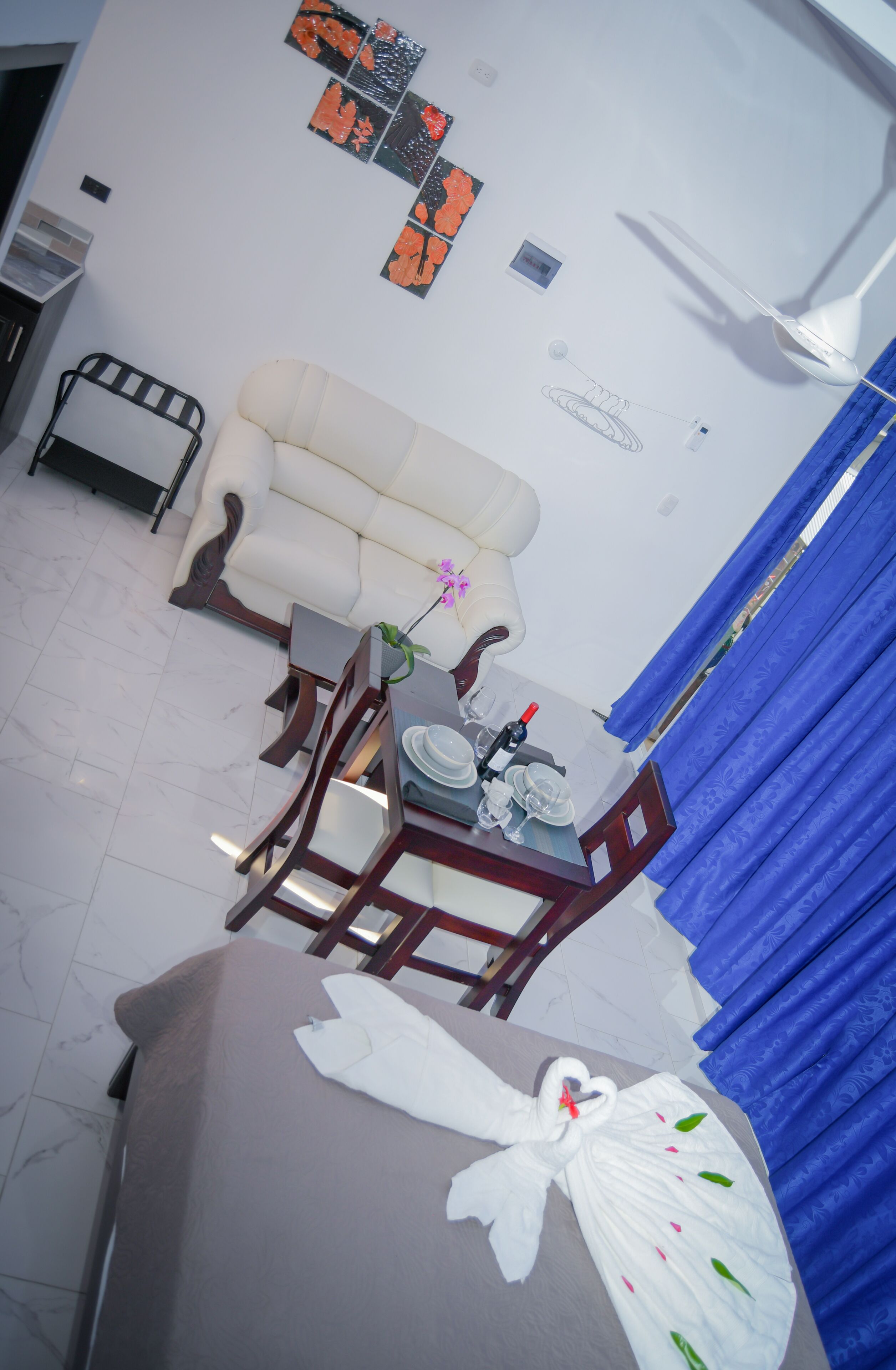A hotel room with a bed, a dining table with chairs, a sofa, and a small table with a vase of flowers.