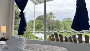 A hotel room with a bed, a window with blue curtains, and a view of greenery outside. - Hotel Serendipity tortuguero (Colorado)