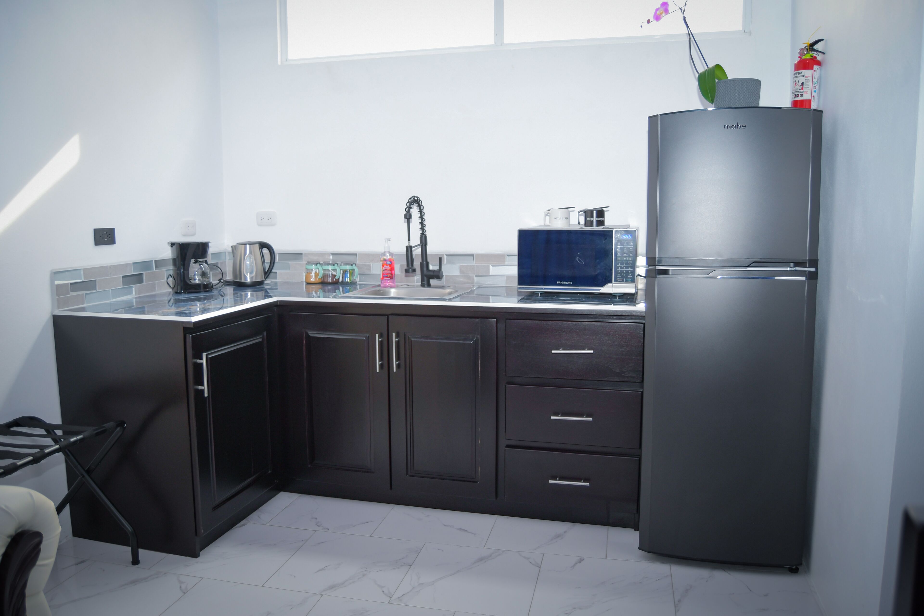 A modern kitchen with dark cabinets, a stainless steel refrigerator, a coffee maker, and a microwave.