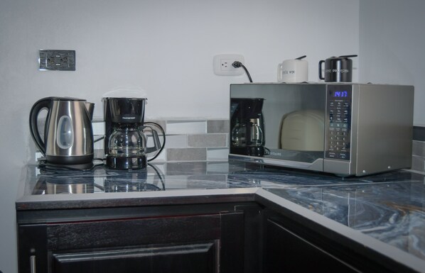 A kitchen with a coffee maker, a kettle, and a microwave on a marble countertop.