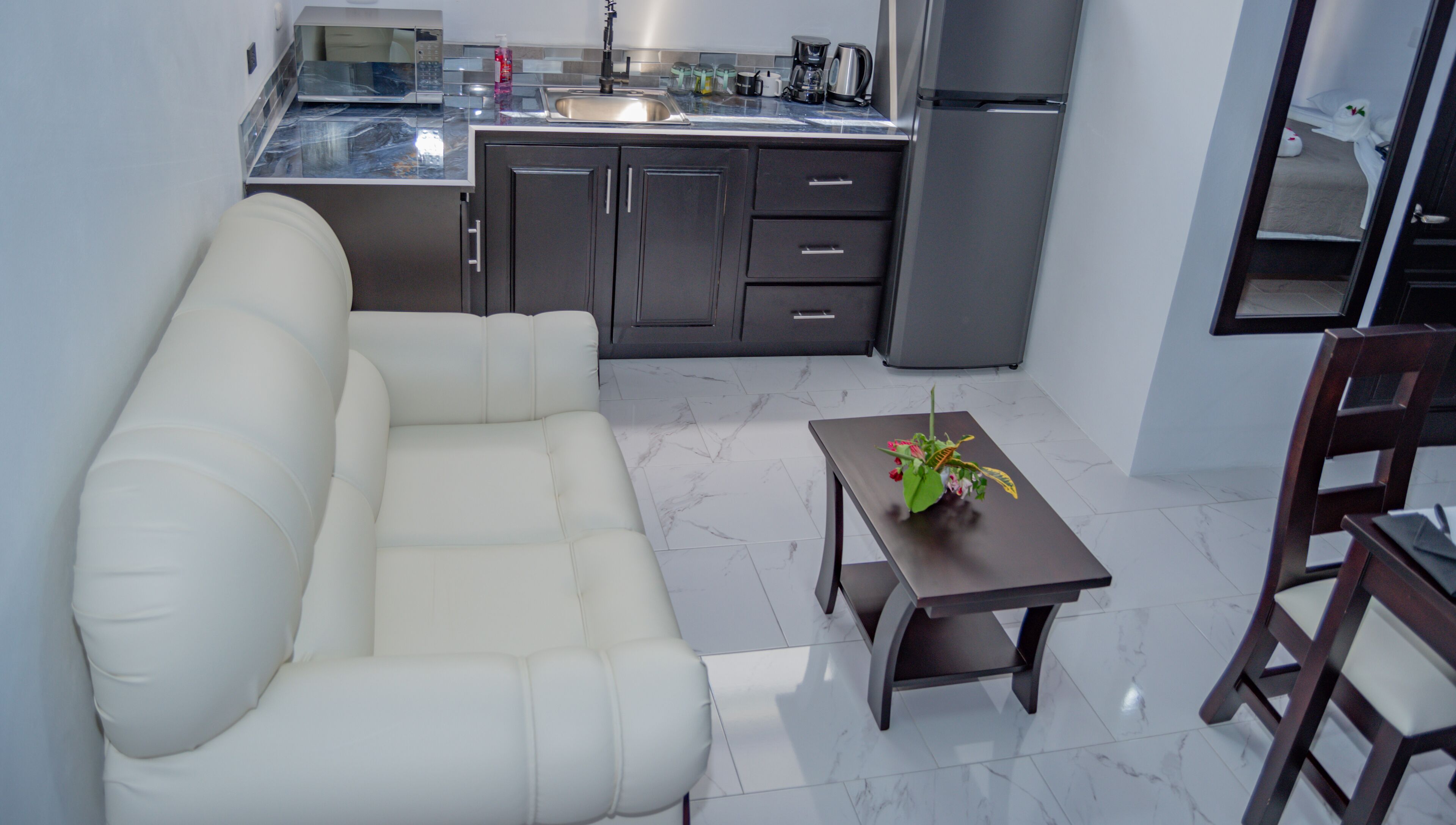 A modern kitchen with dark cabinets, a white sofa, and a small table with a flower vase.