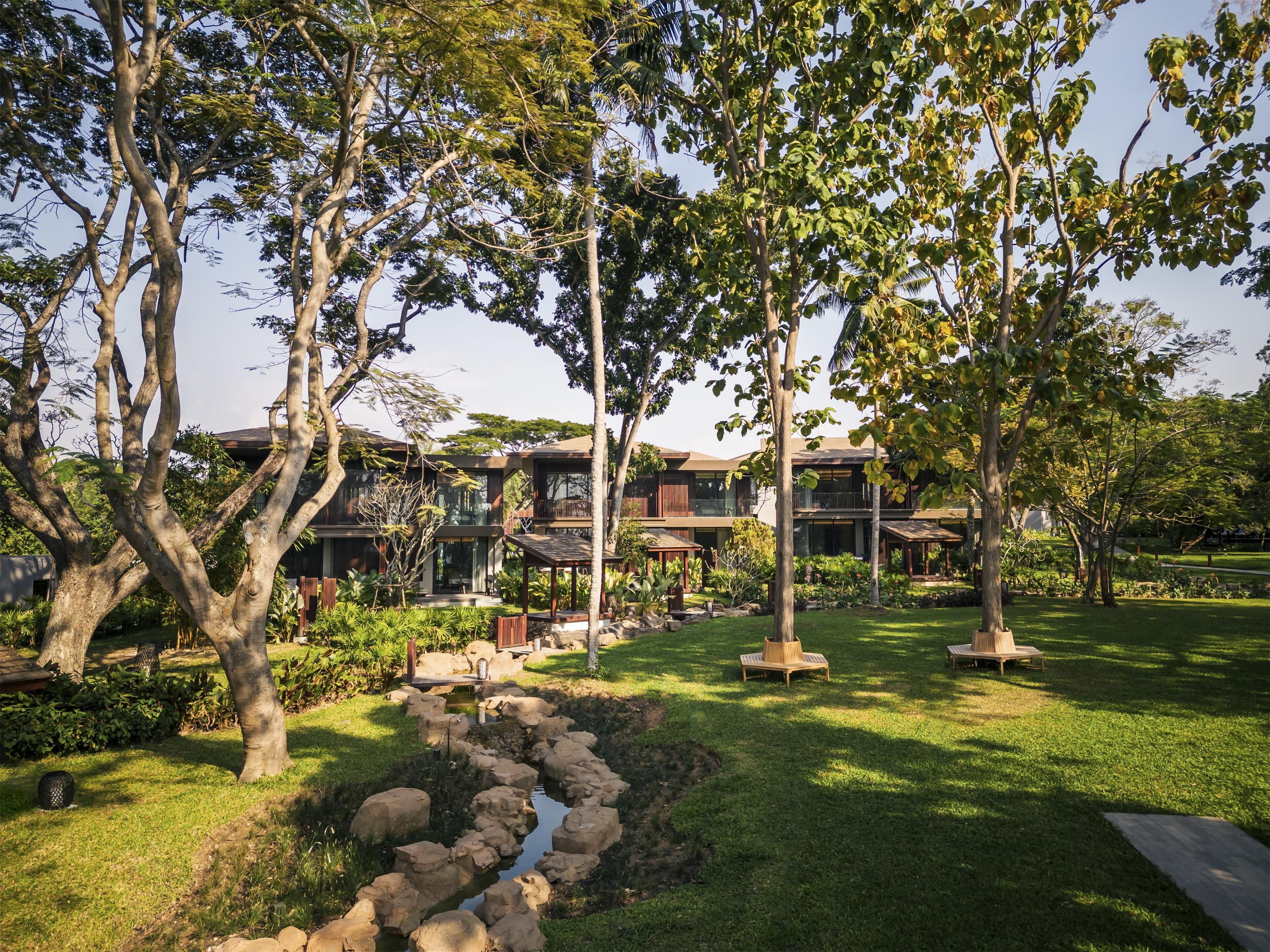 A modern multi-story building with a well-maintained garden, including a small stream and seating areas.