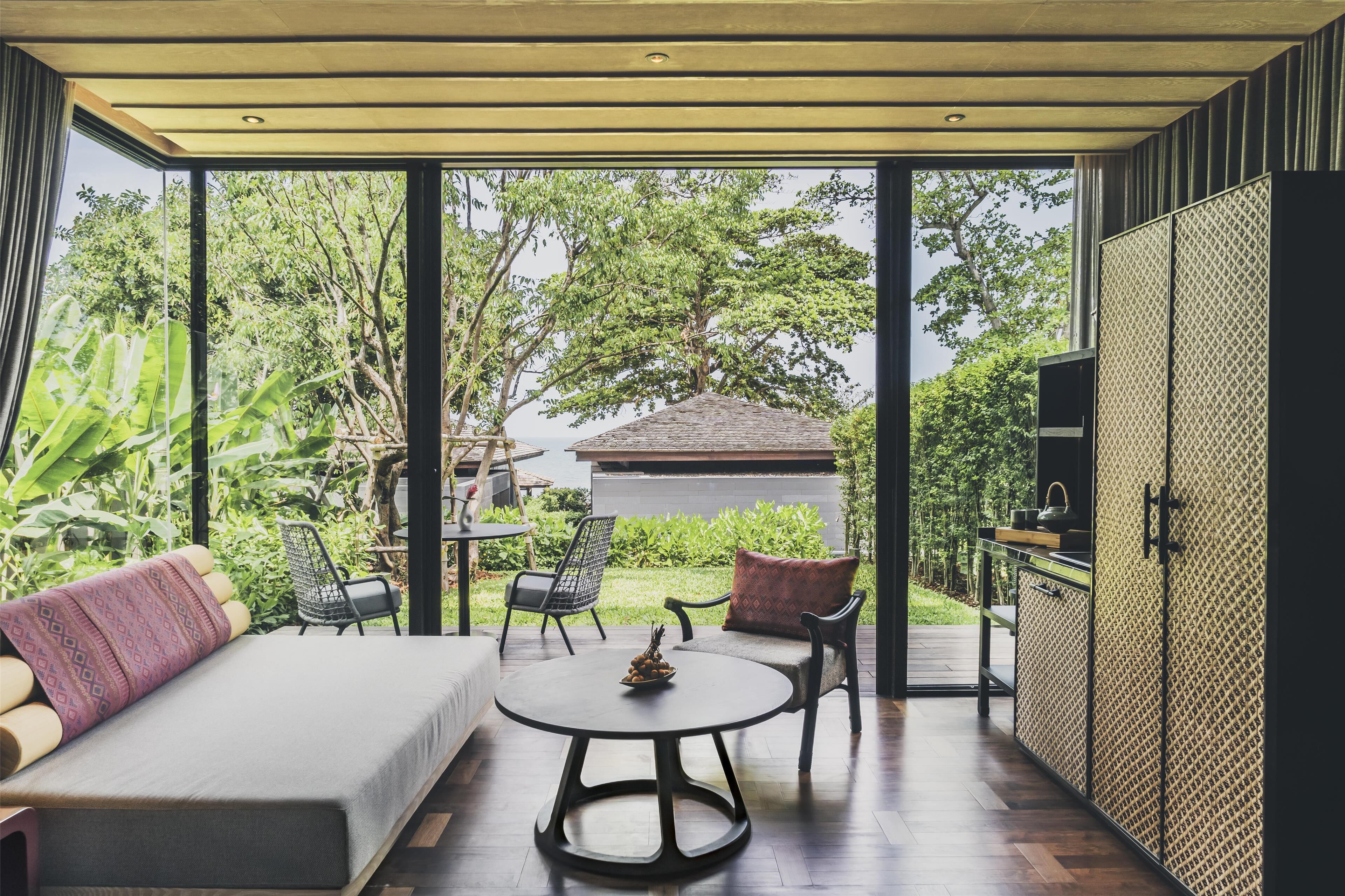 A modern room with a sofa, a round table, and chairs, a TV, and a view of greenery outside.