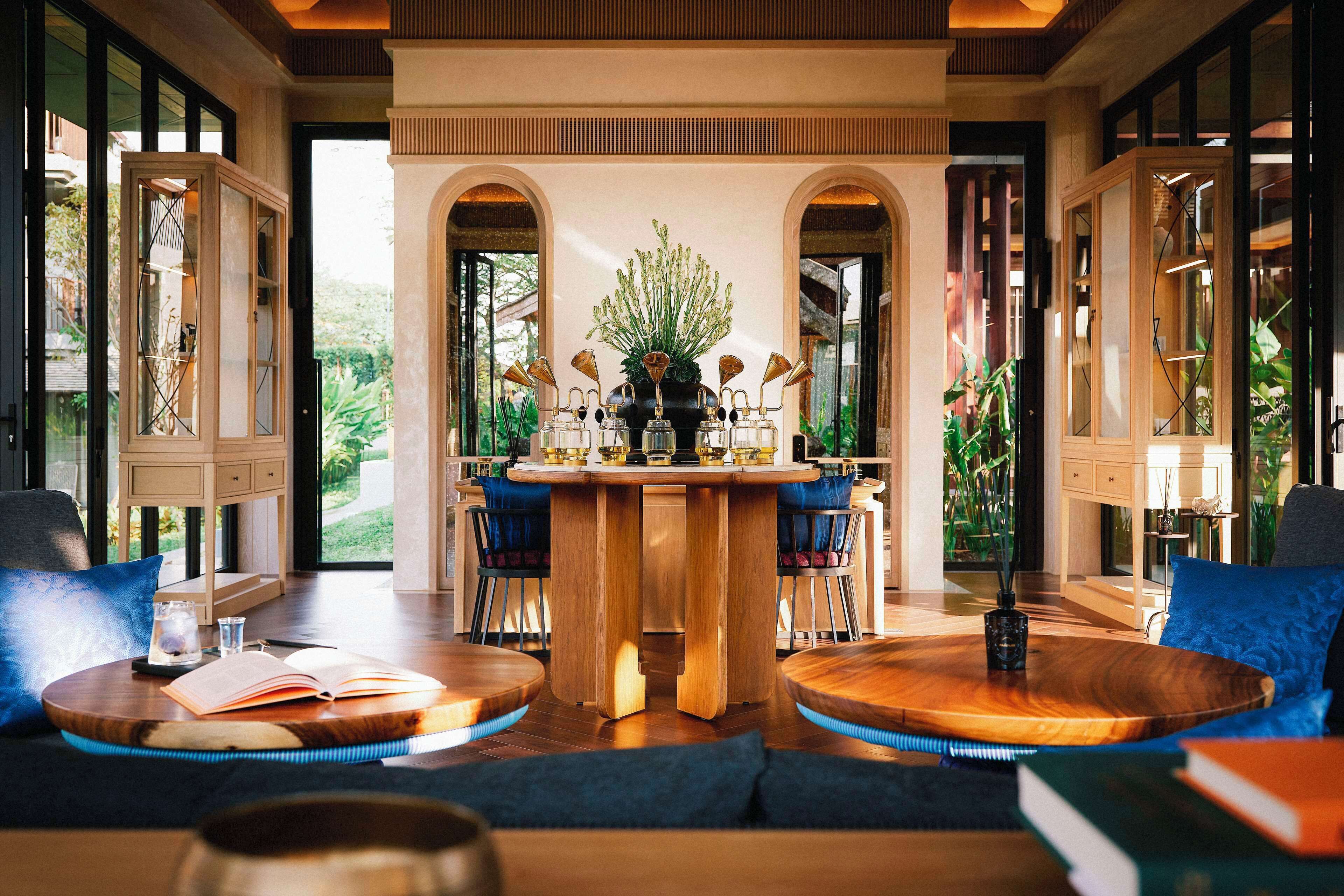 Une pièce spacieuse avec une grande table à manger en bois, entourée de chaises, d’un canapé et d’une table basse. Au centre, on trouve une bibliothèque et une plante en pot.