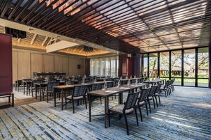 A spacious conference room with long tables and chairs, large windows, and a high ceiling with wooden beams.