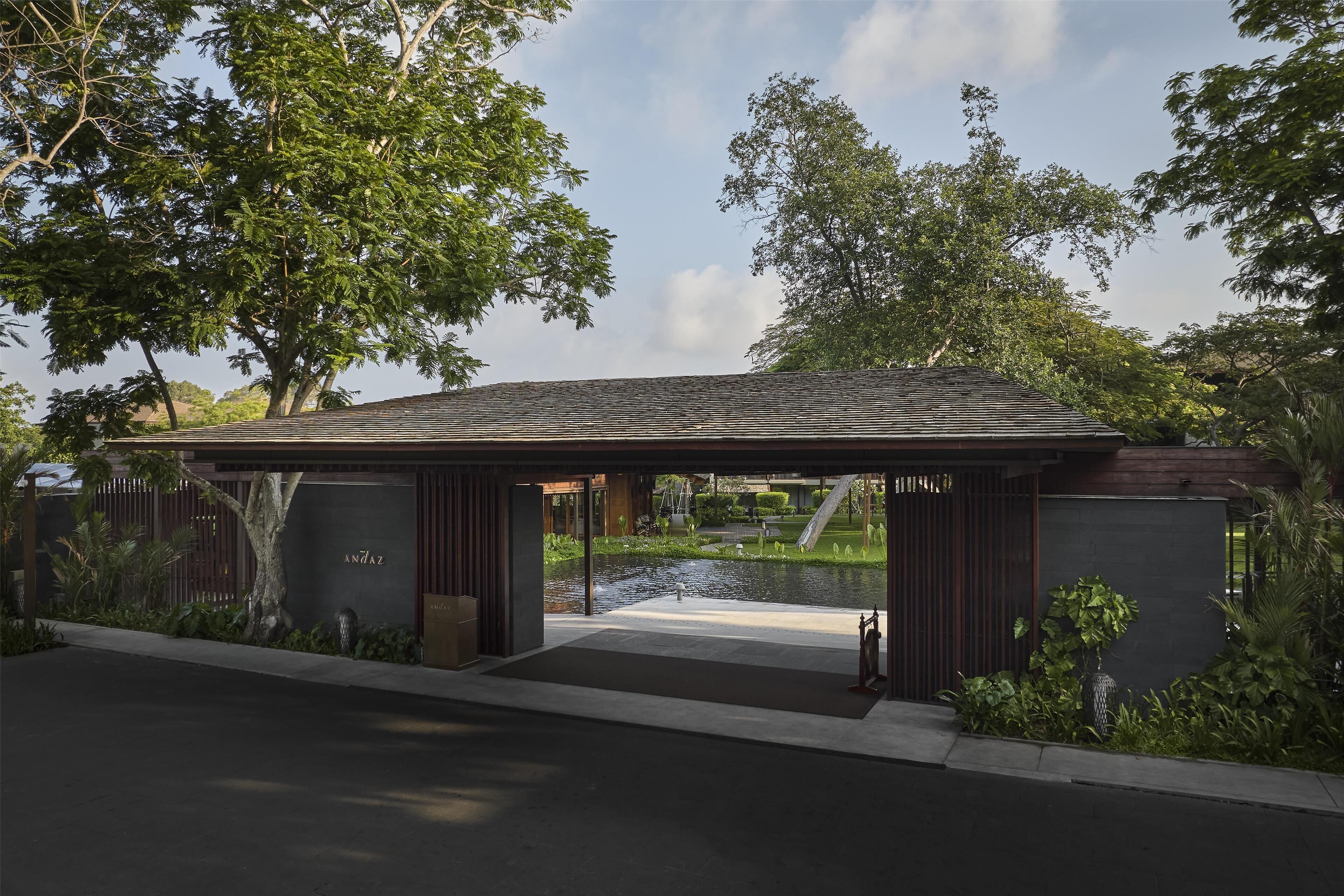 A modern building with a covered entrance, a small pond, and lush greenery.