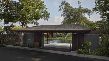A modern building with a covered entrance, a small pond, and lush greenery.