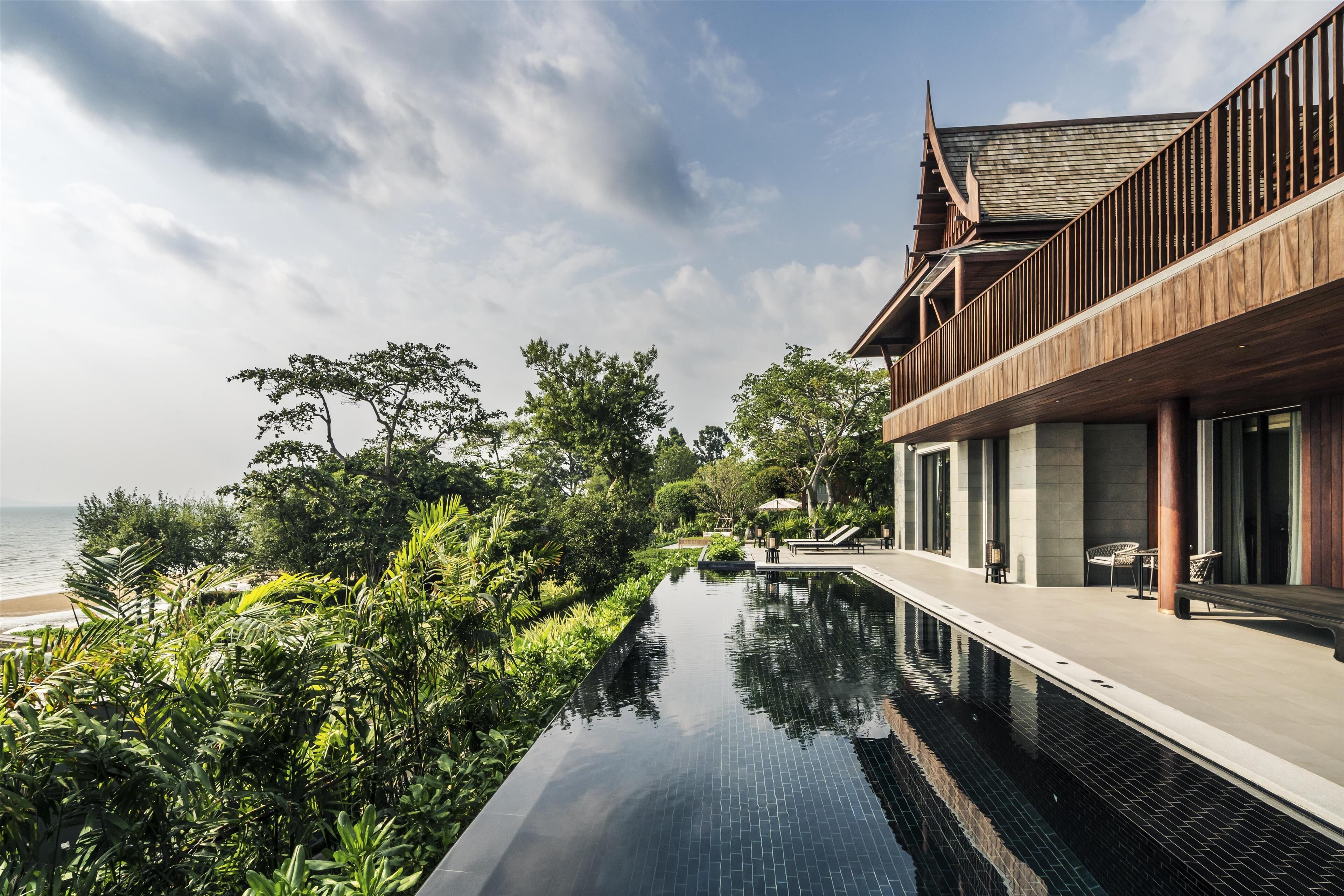 A modern hotel with a pool overlooking the sea, featuring a wooden deck and lush greenery.