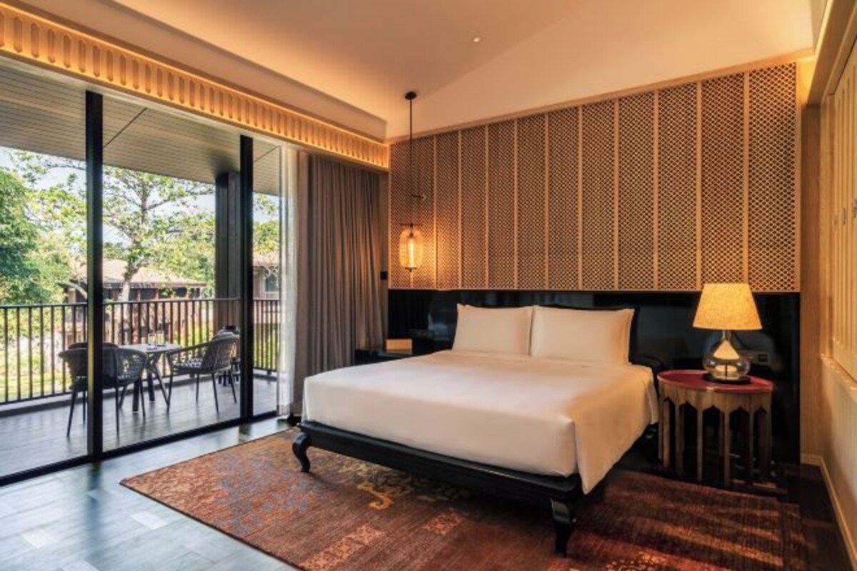 Une chambre d’hôtel moderne dotée d’un grand lit, d’un balcon avec mobilier d’extérieur et offrant une vue sur la verdure.