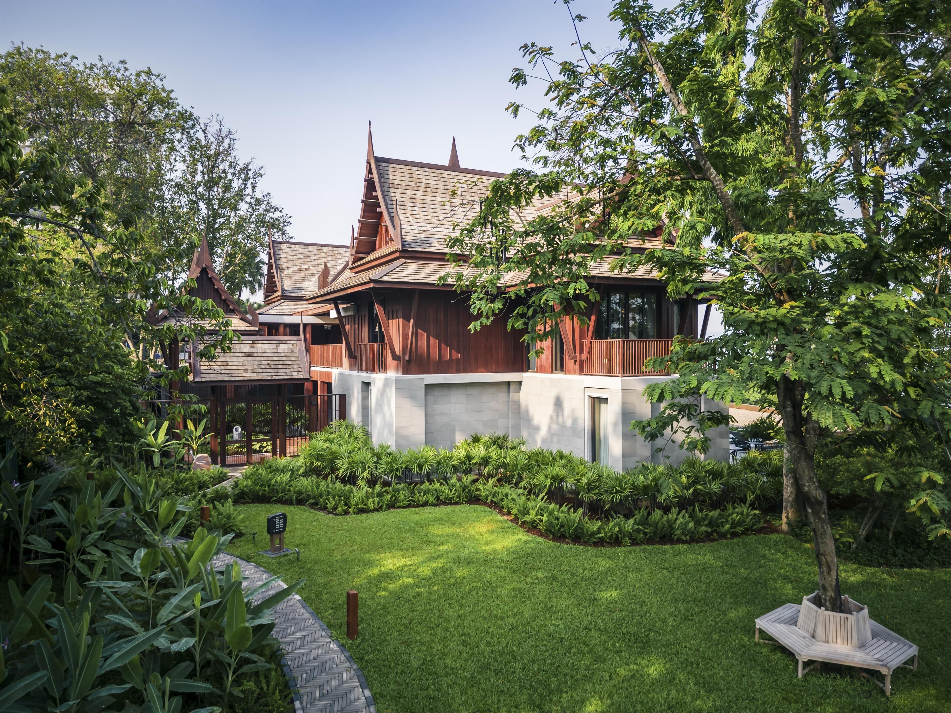 A traditional wooden house with a sloped roof, surrounded by lush greenery and a well-maintained lawn.