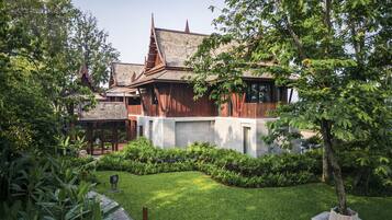 A traditional wooden house with a sloped roof, surrounded by lush greenery and a well-maintained lawn.