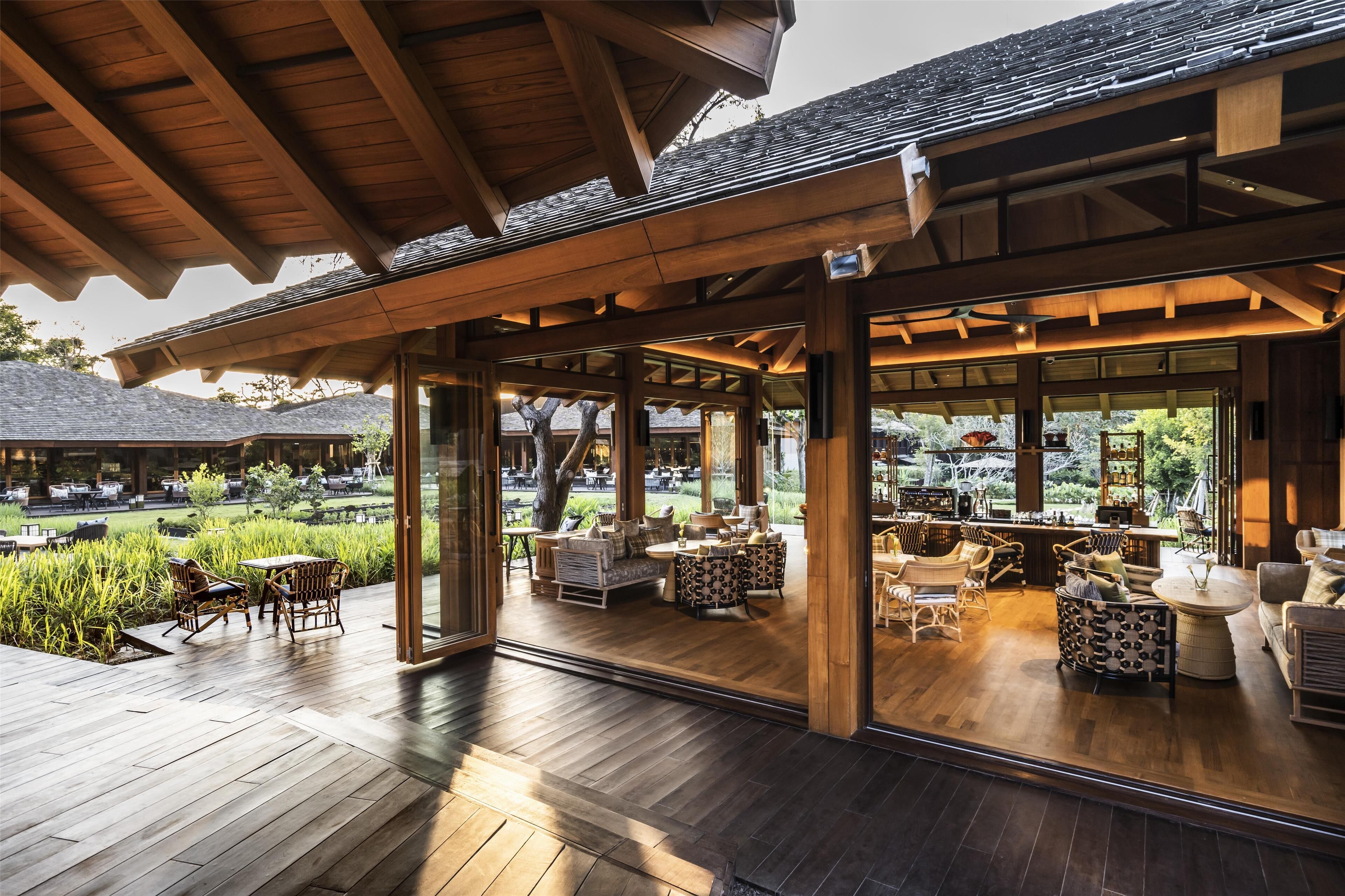 An outdoor patio area with wooden flooring, wicker furniture, and a view of a garden.