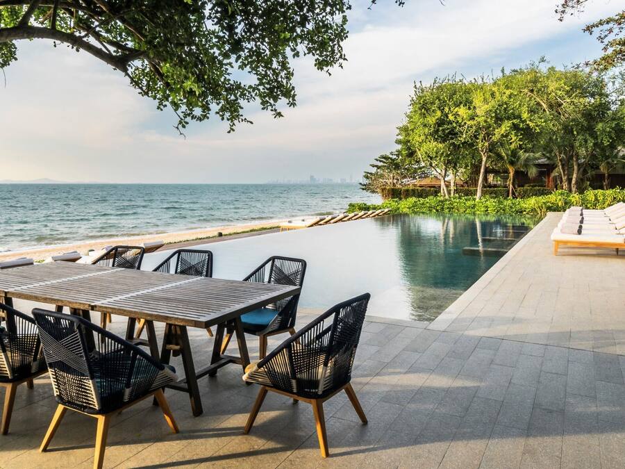 A poolside area with a table and chairs, a lounge with sun loungers, and a view of the ocean.
