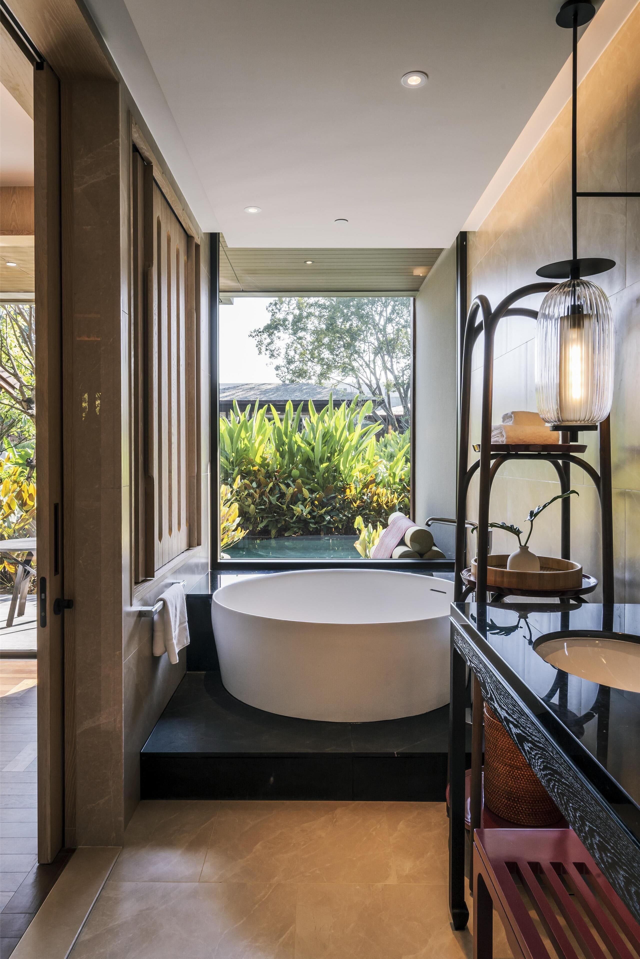 A modern bathroom with a freestanding bathtub, a glass-enclosed shower, and a wooden shelf with a lamp.