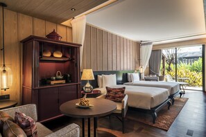Een hotelkamer met twee bedden, een houten kast, een tafel met fruit en uitzicht op groen door grote ramen.