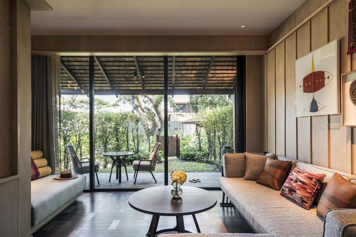 Un salon moderne avec un canapé, une table basse et une vue sur un jardin luxuriant, visible à travers de grandes portes vitrées.
