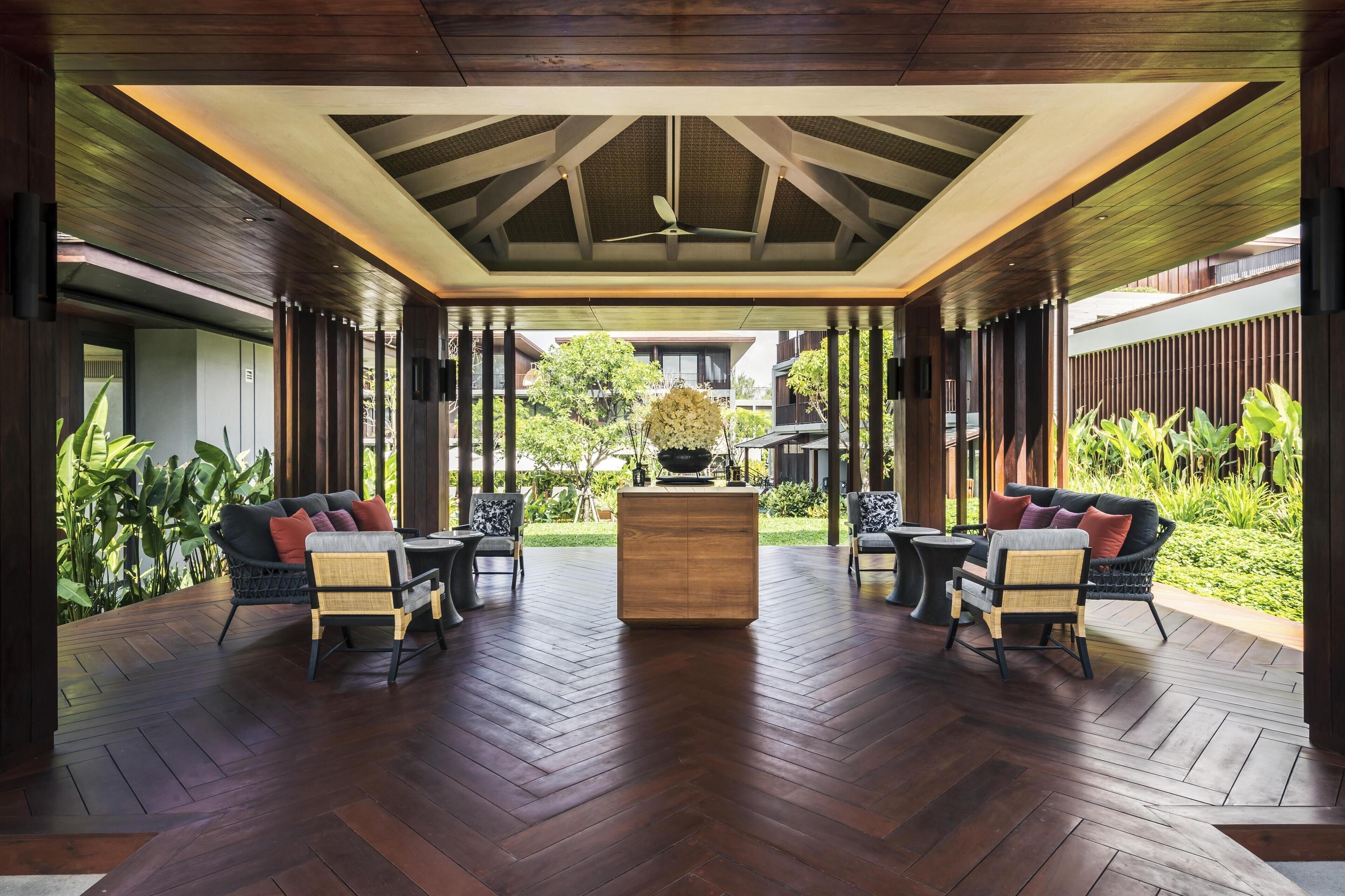 A covered outdoor seating area with wooden flooring, two sofas, and a central table.