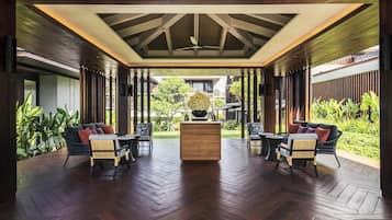 A covered outdoor seating area with wooden flooring, two sofas, and a central table.