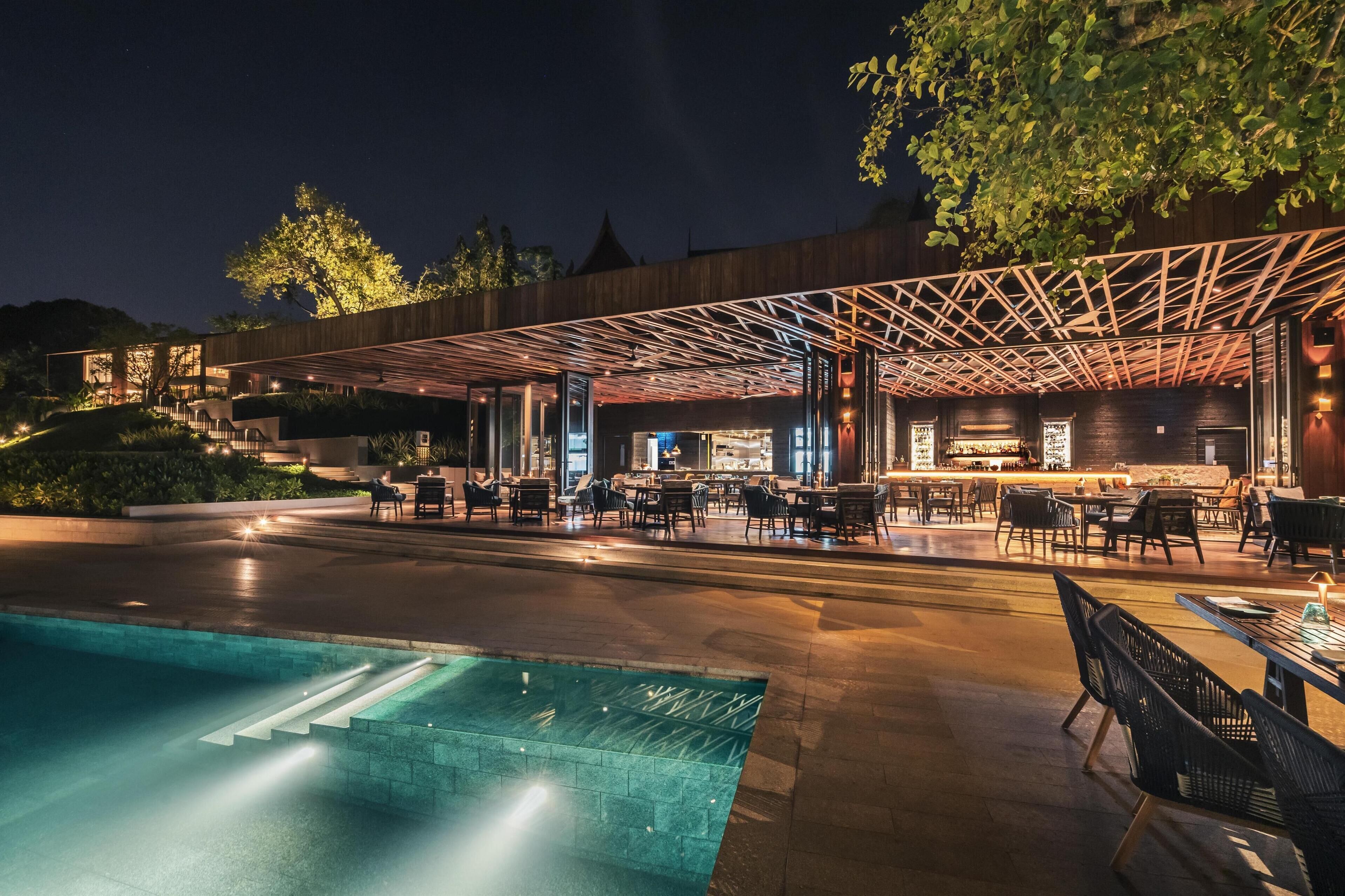 An outdoor dining area with a pool, wooden pergola, and a bar.