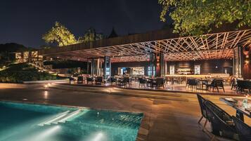 An outdoor dining area with a pool, wooden pergola, and a bar.