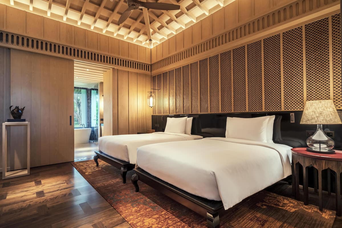 Une chambre d’hôtel avec deux lits, un plancher en bois, un mur décoré d’un motif et un ventilateur de plafond.