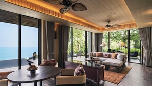 Een ruime woonkamer met een groot raam met uitzicht op zee, een plafondventilator en een gezellige zithoek met een bank en stoelen.