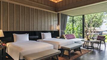 A hotel room with two beds, a sofa, a small table, and a view of greenery outside.