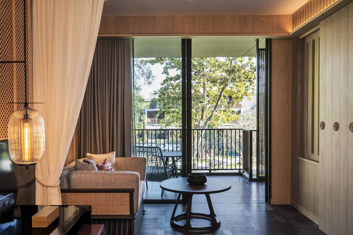 Une chambre d’hôtel moderne dotée d’un balcon, d’un canapé, d’une table et d’un luminaire suspendu.