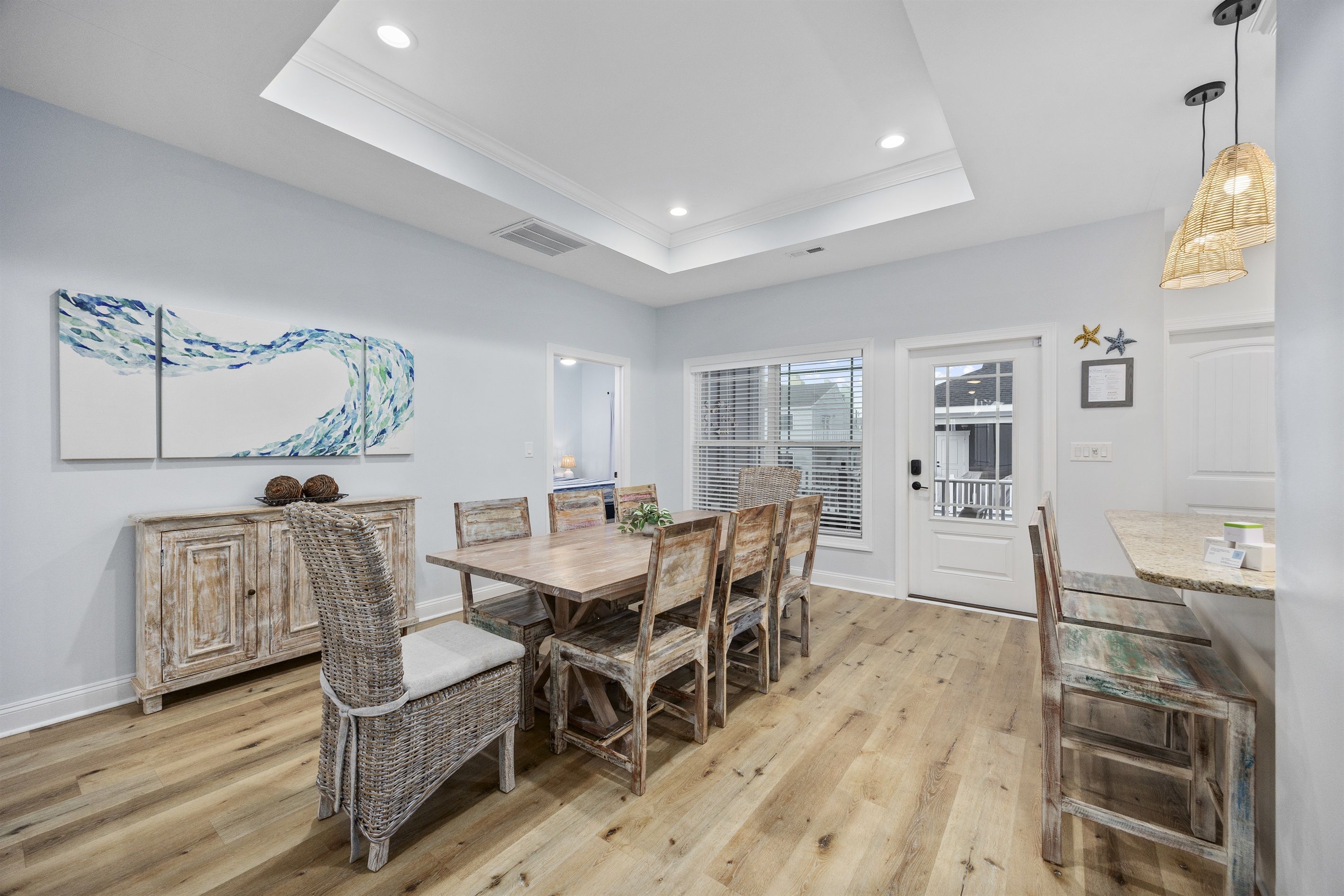 A dining area with a wooden table and chairs, a white ceiling, and a view to the outside.