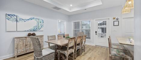 A dining area with a wooden table and chairs, a white ceiling, and a view to the outside.