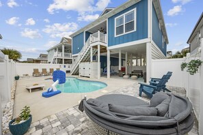 A backyard with a swimming pool, a covered seating area, and a staircase leading to a deck. - Heated Pool | 2 Min to Beach | Dogs Welcome (North Myrtle Beach)