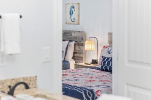 A hotel room with a wooden headboard, a patterned bedspread, a bedside lamp, and a seahorse artwork on the wall. - Heated Pool | 2 Min to Beach | Dogs Welcome (North Myrtle Beach)