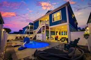 Una casa de dos pisos con piscina, mobiliario exterior y una escalera que conduce a la planta superior.