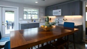A modern kitchen with grey cabinets, a wooden dining table, and a fruit bowl.