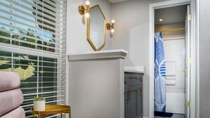 A hallway with a white wall, a gold-framed mirror, and a small table with a plant.