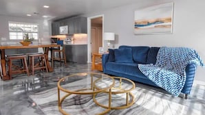 A modern living room with a blue sofa, a coffee table, and a kitchen in the background.