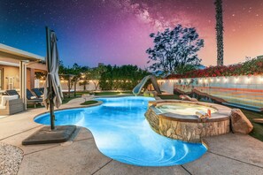 Ein Schwimmbecken mit Whirlpool, umgeben von einer Steindeck, Palmen und einem Sternenhimmel.
