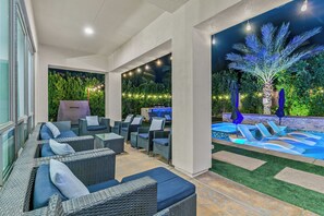 An outdoor patio with wicker furniture, a grill, and a pool area with palm trees.