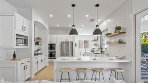 A modern kitchen with white cabinetry, stainless steel appliances, and a central island with bar stools. - The Montage: Luxury Resort Desert Retreat (Indio)