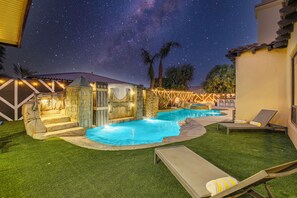 A backyard with a swimming pool, artificial grass, and lounge chairs.