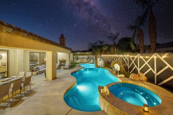 A swimming pool with a hot tub, a covered patio area, and a view of the night sky.