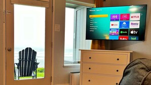 Un salón con televisor mostrando la interfaz de Roku, una ventana con vista al océano, una silla y un aparador de madera.