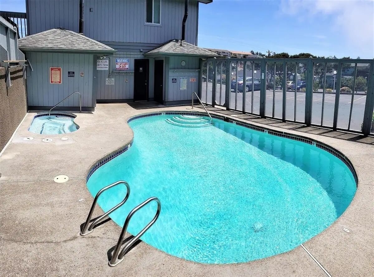 Una piscina con un jacuzzi pequeño, zona cubierta y aparcamiento vallado.