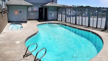 Una piscina con un jacuzzi pequeño, zona cubierta y aparcamiento vallado.