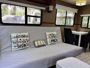 Ein gemütliches Interieur mit einer Couch, die mit reisebezogenen Kissen dekoriert ist, einem Tisch und einem Fenster mit Blick nach draußen.