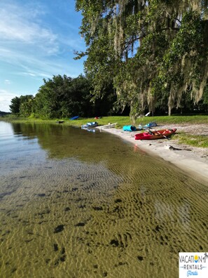 Ein Strand mit Kajaks und einem Boot, klares, flaches Wasser und Bäume mit spanischem Moos.