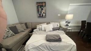 A bedroom with a bed, a sofa, a lamp, and a poster on the wall.
