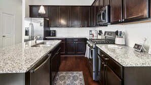 A kitchen with dark wood cabinets, granite countertops, stainless steel appliances, and a hanging pendant light.